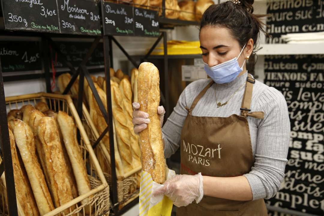Продавец кладет багет в бумажный пакет