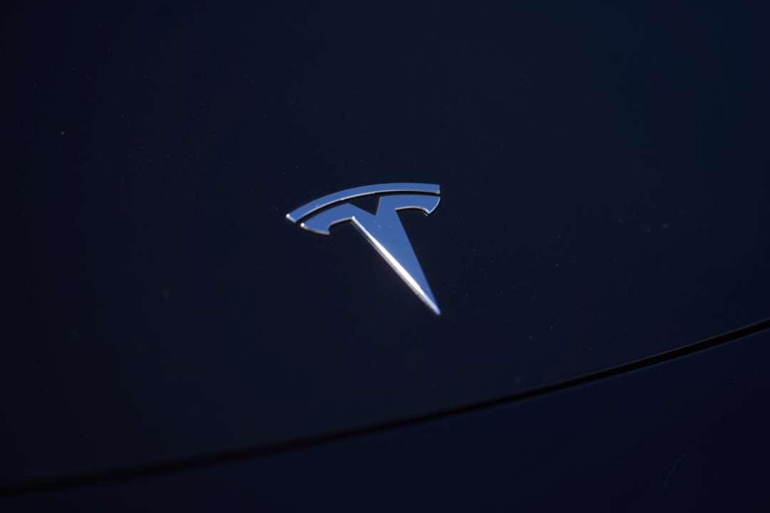 Tesla отзывает более миллиона автомобилей из-за проблем с окнами/Фото: Allison Dinner/Getty Images Логотип Tesla на капоте черного автомобиля